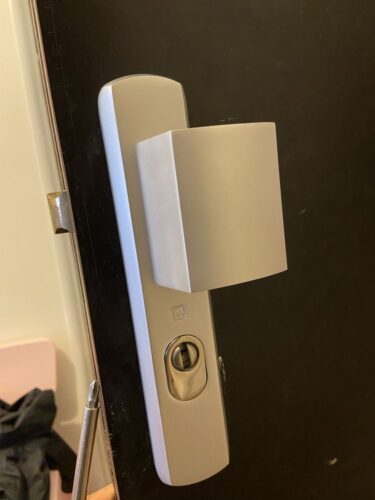 Close-up of a modern silver door lever and deadbolt on a dark door, with a screwdriver nearby.
