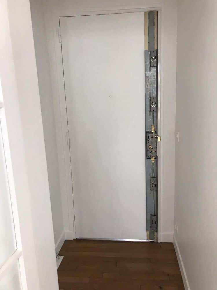 White interior door in a narrow hallway with an exposed metal security frame and multiple lock mechanisms on the right edge.